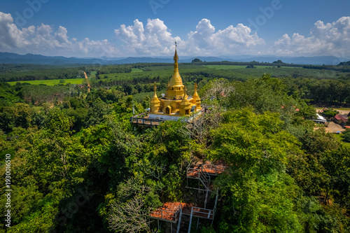 Aerial drone view of golden pagoda at Wat Prangkasi in Thong Pha Phum, Kanchanaburi, Thailand surrounded by lush forest mountain landscape