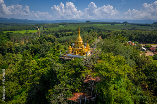 Aerial drone view of golden pagoda at Wat Prangkasi in Thong Pha Phum, Kanchanaburi, Thailand surrounded by lush forest mountain landscape