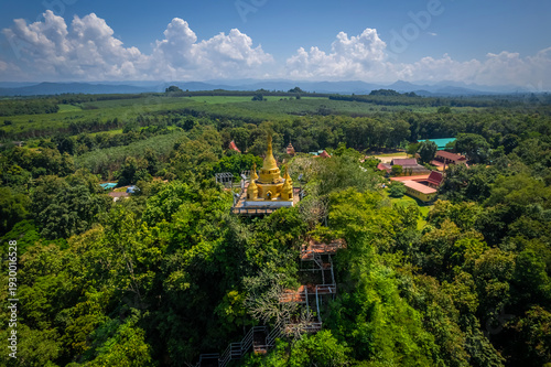 Aerial drone view of golden pagoda at Wat Prangkasi in Thong Pha Phum, Kanchanaburi, Thailand surrounded by lush forest mountain landscape
