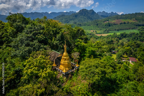 Aerial drone view of golden pagoda at Wat Prangkasi in Thong Pha Phum, Kanchanaburi, Thailand surrounded by lush forest mountain landscape