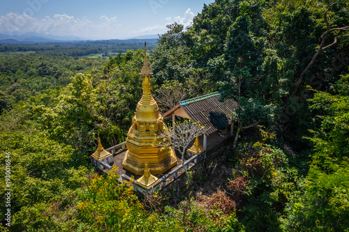 Aerial drone view of golden pagoda at Wat Prangkasi in Thong Pha Phum, Kanchanaburi, Thailand surrounded by lush forest mountain landscape