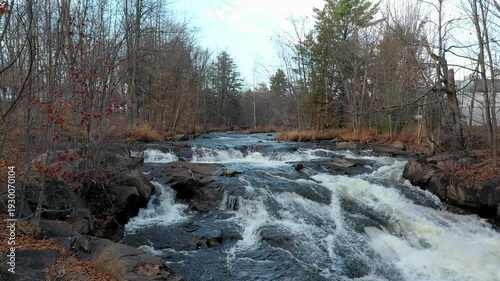 Drone flying at low altitude over the rivers with rapids staying still and showing the small waterfalls with colorful trees in the Fall