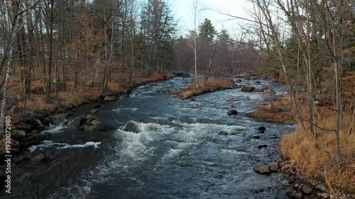 Drone flying at low altitude over the rivers with rapids moving backwards over the small waterfalls with colorful trees in the Fall