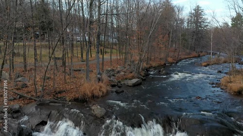 Moving forward filming straight down and while flying, revealing the surrounding scenery of the river with the trees in the Fall.