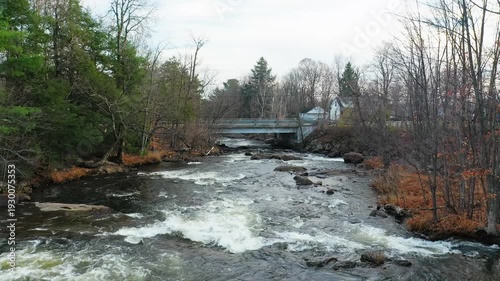 Crane shot with a drone, coming down over the river, near the small bridge in the village, passing over the rapids in Fall.