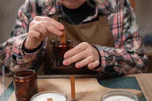 Fotografija Candle maker putting wooden wick into glass jar in workshop