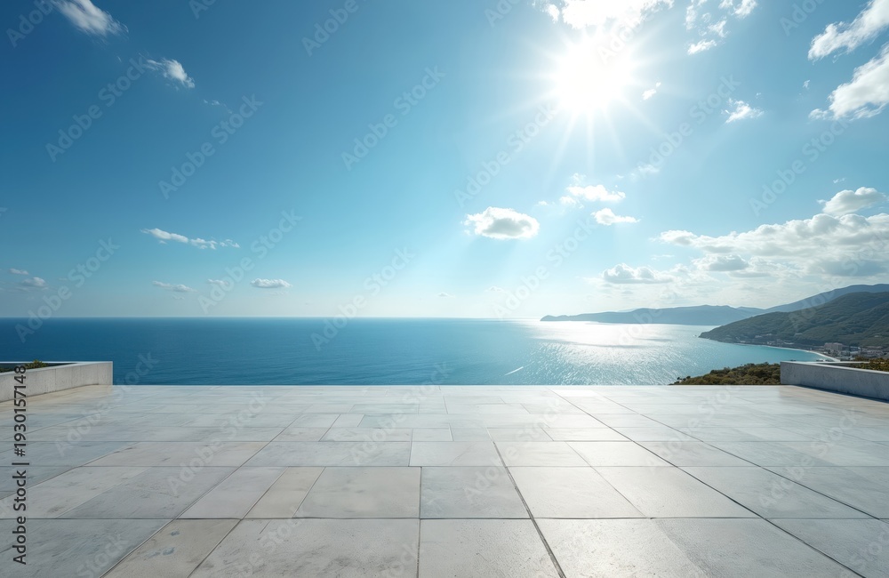 Fototapeta premium Large tiled terrace overlooks calm blue sea under sunny sky. Coastal landscape with distant hills and buildings features bright ocean horizon, perfect for vacation and travel themes.