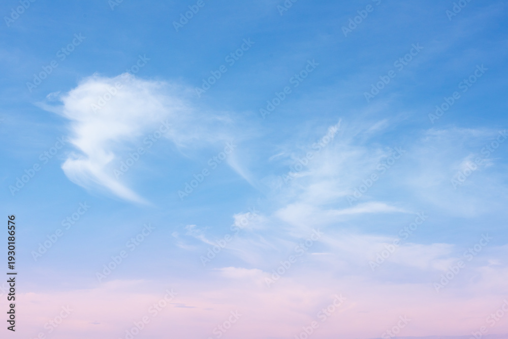 Fototapeta premium Soft blue sky with delicate white cirrus cloud wisps and pale pink horizon creating calm serene atmosphere at sunrise or sunset