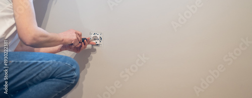 Tableau sur toile Man crouching installing a new electrical outlet into a light-colored wall using