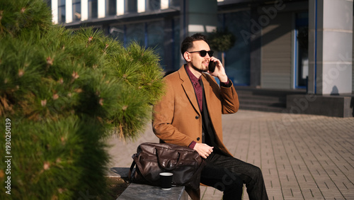 Young male businessman talking on smartphone in business center parking lot