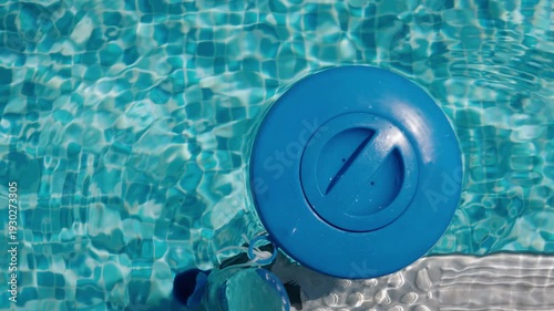 Floating chlorine dispenser in clear swimming pool water with sunlight reflections