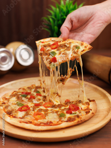 Small homemade frozen pizza toppings minced meat spicy chili sauce stretching melty cheese golden yellow color on wooden board tasty food fresh delicious cuisine gourmet italian style thin crust.