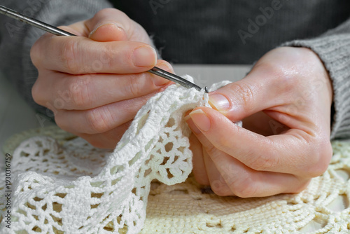 A woman crochets a napkin. Top view, close-up.