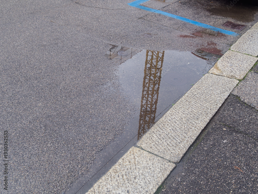 Fototapeta premium Reflection of a construction crane in a puddle on an asphalt surface with stone curb