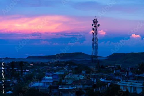 Cherrapunji, India - 25 July 2023: View of the towering telecommunications tower piercing through the vibrant twilight sky above the misty town.