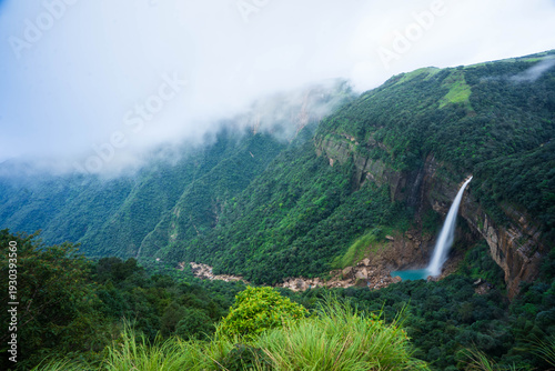 Cherrapunji, India - 27 July 2023: View of the majestic Nohkalikai Falls plunging from lush green cliffs into a turquoise pool, shrouded in mystic clouds, creating a breathtaking vista.