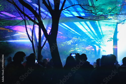 Lasers at music festival with people shadows and hands with smartphones in the air