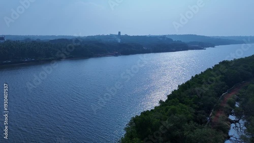 A calm river flows gently through lush green trees and open land. Birds sing softly while the clear water reflects the sky, creating a peaceful and beautiful scene in nature.