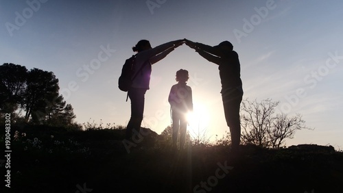 Valokuva Family figures form a house shape with arms around a child, silhouetted against