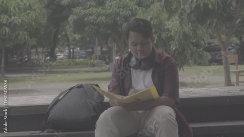 A Southeast Asian student studies in the campus yard alone with books and a tablet. S-Log3, S-Gamut3.Cine