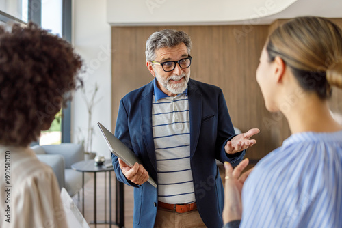 Smiling businessman carrying laptop sharing new ideas with female coworkers during collaborative discussion in office