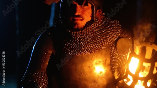 A knight in full armor, holding a sword and torch, stands in a dark night forest. A medieval warrior searches in the darkness.