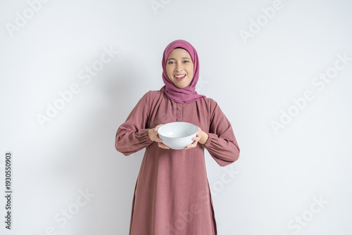 Obraz na płótnie Portrait of a smiling Asian Muslim woman in pink hijab holding a white ceramic bowl with both hands
