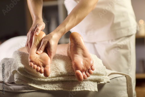Massage therapist treats client feet with relaxation. Hands apply oil on foot soles in a spa with towels and candles, ideal for reflexology treatment. Calm restorative care concept for wellness.