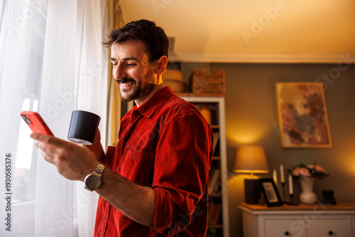 Man drinking coffee and using smart phone while relaxing at home