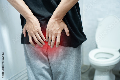 Photos Man suffering from hemorrhoids or rectal pain holding his buttocks in bathroom