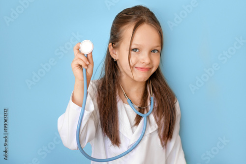 A funny girl in a white coat in the guise of a pediatrician holds a stethoscope. Pediatric cardiology, diseases of the heart and cardiovascular system