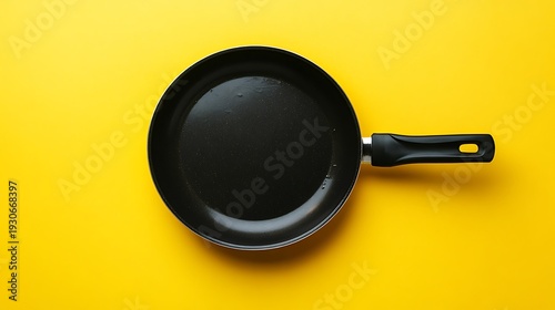 A black non stick frying pan with handle on yellow background