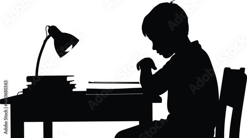 Young boy diligently studies at a wooden desk illuminated by a focused desk lamp in the dark room.