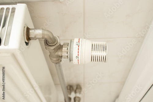 Radiator thermostat valve on heating system in home interior. Temperature regulation, energy efficiency, heating control, utility costs, winter home heating concept.