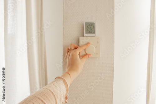 Hand adjusting wall thermostat with digital display in modern interior. Temperature control, smart heating, energy efficiency, home climate management.