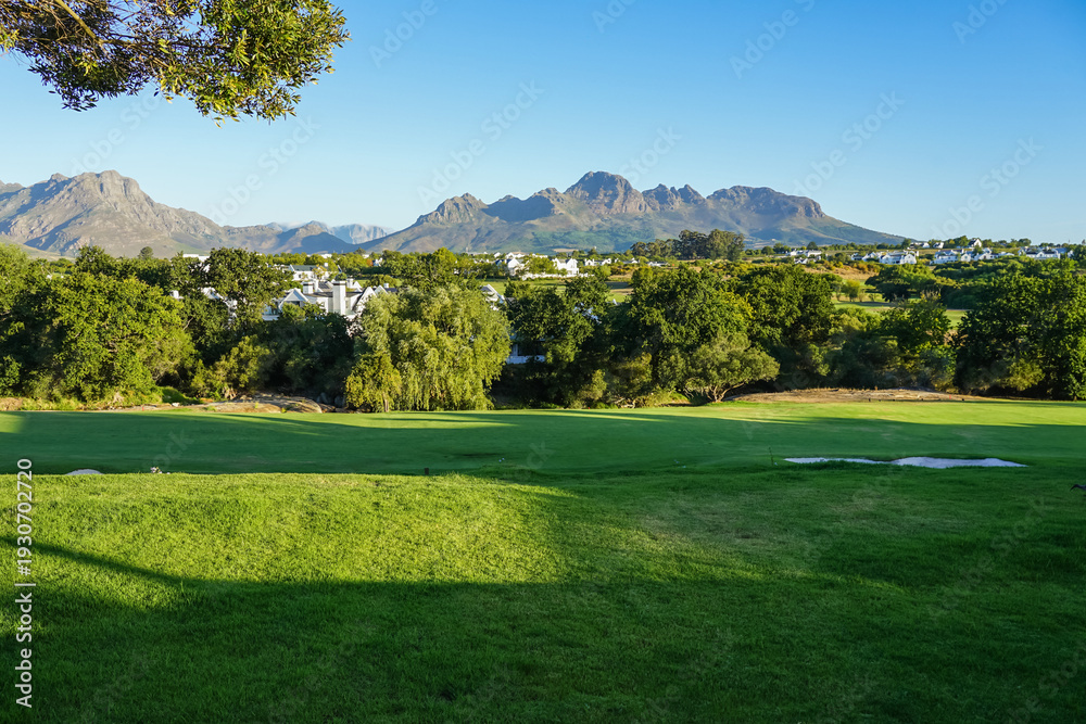 Fototapeta premium South Africa,Winery in Stellenbosch ,A serene golf course with lush green fairways, trees, and distant mountains under a clear blue sky.