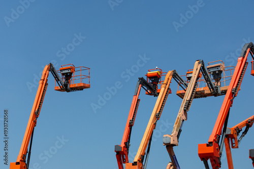 A group of orange and white cranes are in the sky. Mobile construction crane for rent and sale. Aerial work platforms of a cherry pickers with sky background. Boom lifting machine.