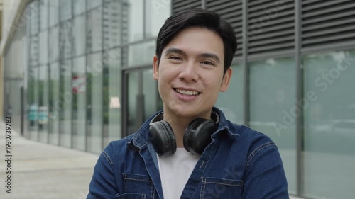 Young Asian man smiles directly at camera, with a building background 