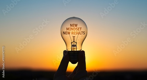 Human hand holding light bulb with text new mindset new results against beautiful sunset sky background for inspiration motivation success and positive thinking concept development