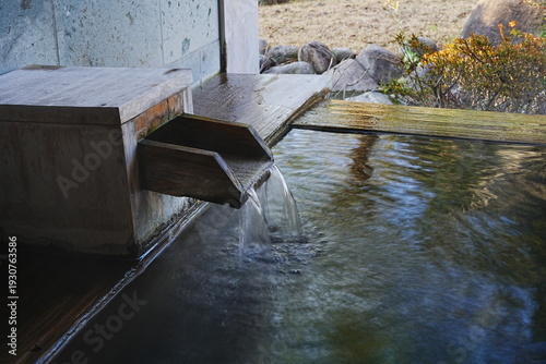 фотографія Traditional Japanese hot spring water flowing from a wooden spout into a bathtub