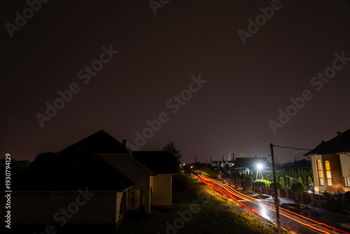Night road with car light trails and suburban lightning