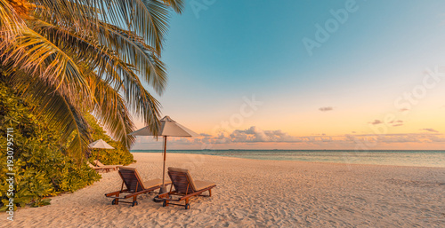 Beautiful tropical sunset scenery with two sun beds loungers umbrella under palm tree white sand sea view horizon colorful twilight sky for inspirational beach resort hotel tourism travel art design