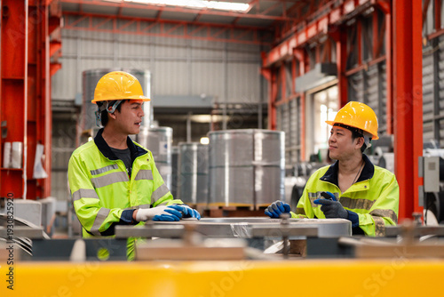 Fényképezés Two industrial engineers in safety helmets using laptop on factory platform, discussing production process in modern manufacturing plant with steel structure and safety compliance concept