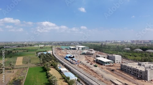 Aerial view of industrial construction site near green fields and cityscape