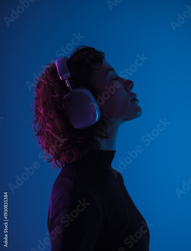 Profile of young woman wearing headphones in blue neon light. Music, focus, technology and modern lifestyle concept.