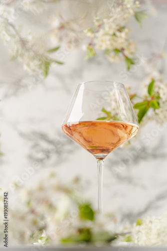 Rose wine glass against white wall with spring cherry flowers. Refreshing alcoholic summer drink or nature concept.