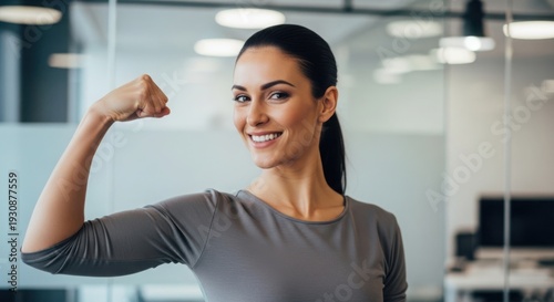 Confident woman flexing her arm in a bright office environment.