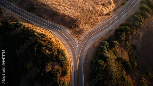 Aerial view of a road forking into two paths during golden hour in a natural landscape