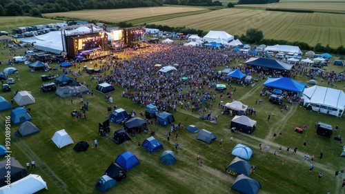 A large crowd gathers at an outdoor music festival with multiple stages set up amid tents and vendors. Attendees enjoy live performances, creating an energetic atmosphere.