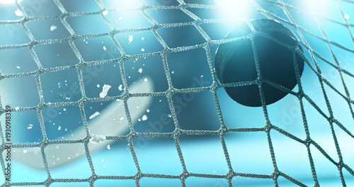 Action sports photo of a hockey puck flying into the goal net during a scoring shot, with ice particles in the air and a hockey stick visible in the background, capturing speed and intensity.